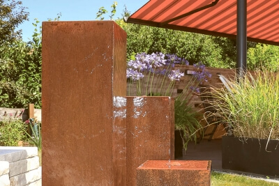 dreisaeuliger-cortenstahlbrunnen-auf-einer-terrasse