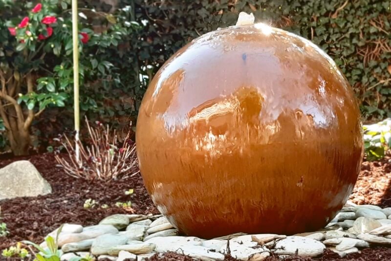 Cortenstahl-Kugelbrunnen in einem Blumenbeet