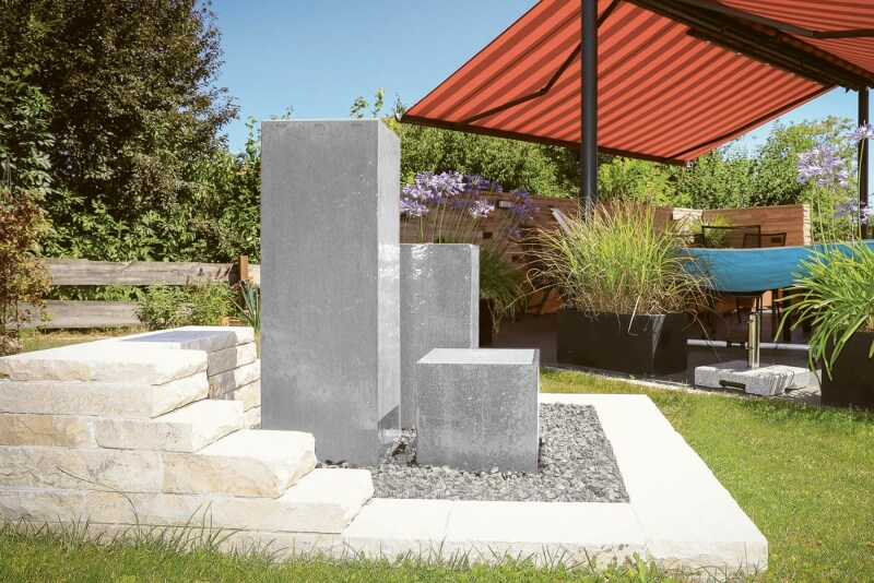 Dreisäuliger Edelstahlbrunnen auf weißem Kies