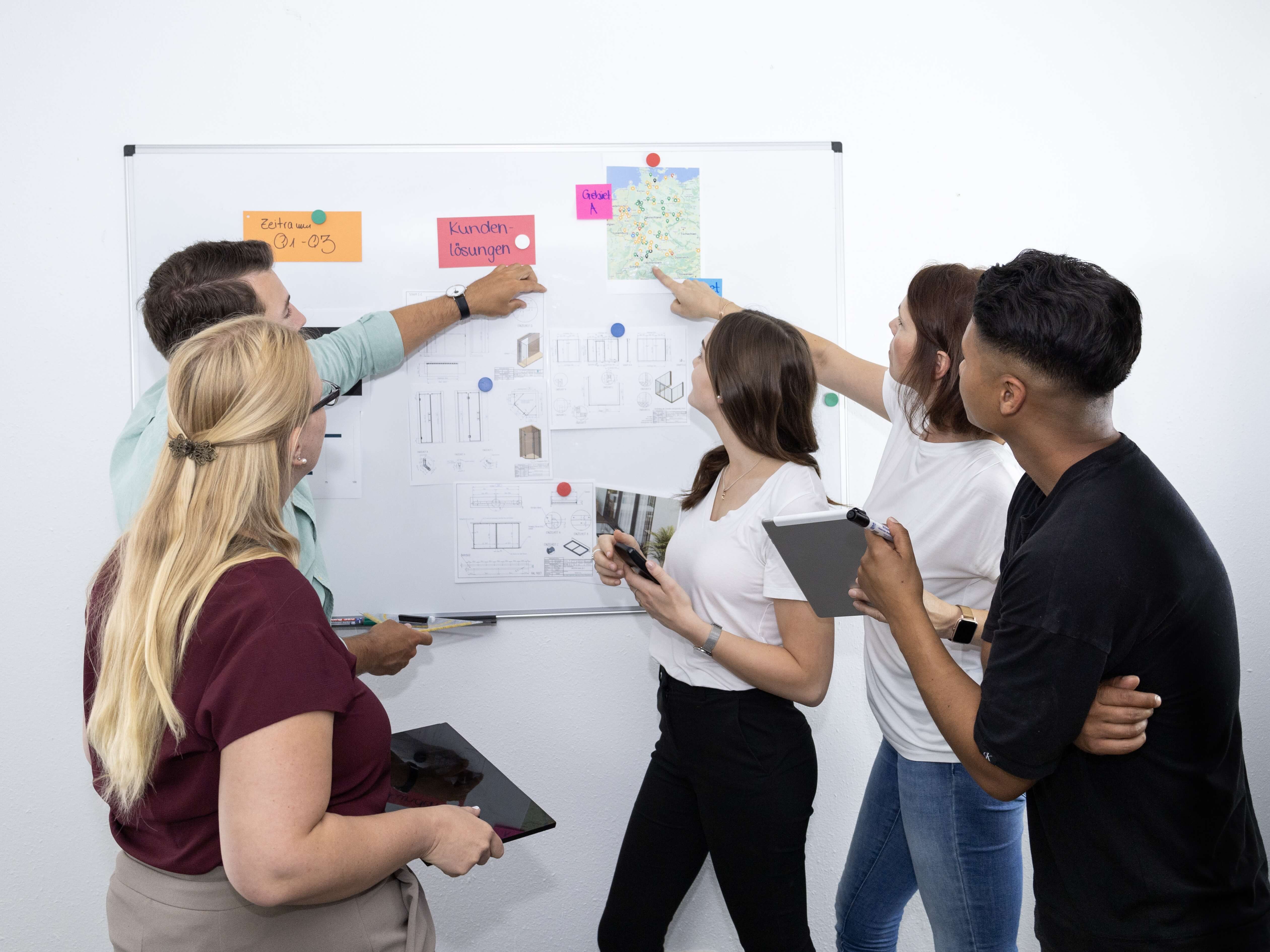 Mitarbeitende diskutieren vor einem Whiteboard